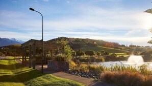 Un parc paisible avec un kiosque, un étang et une chaîne de montagnes en arrière-plan.