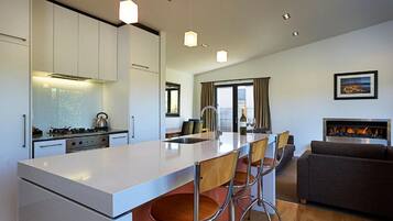 A modern kitchen with a central island, bar stools, a dining area, and a living room with a fireplace.