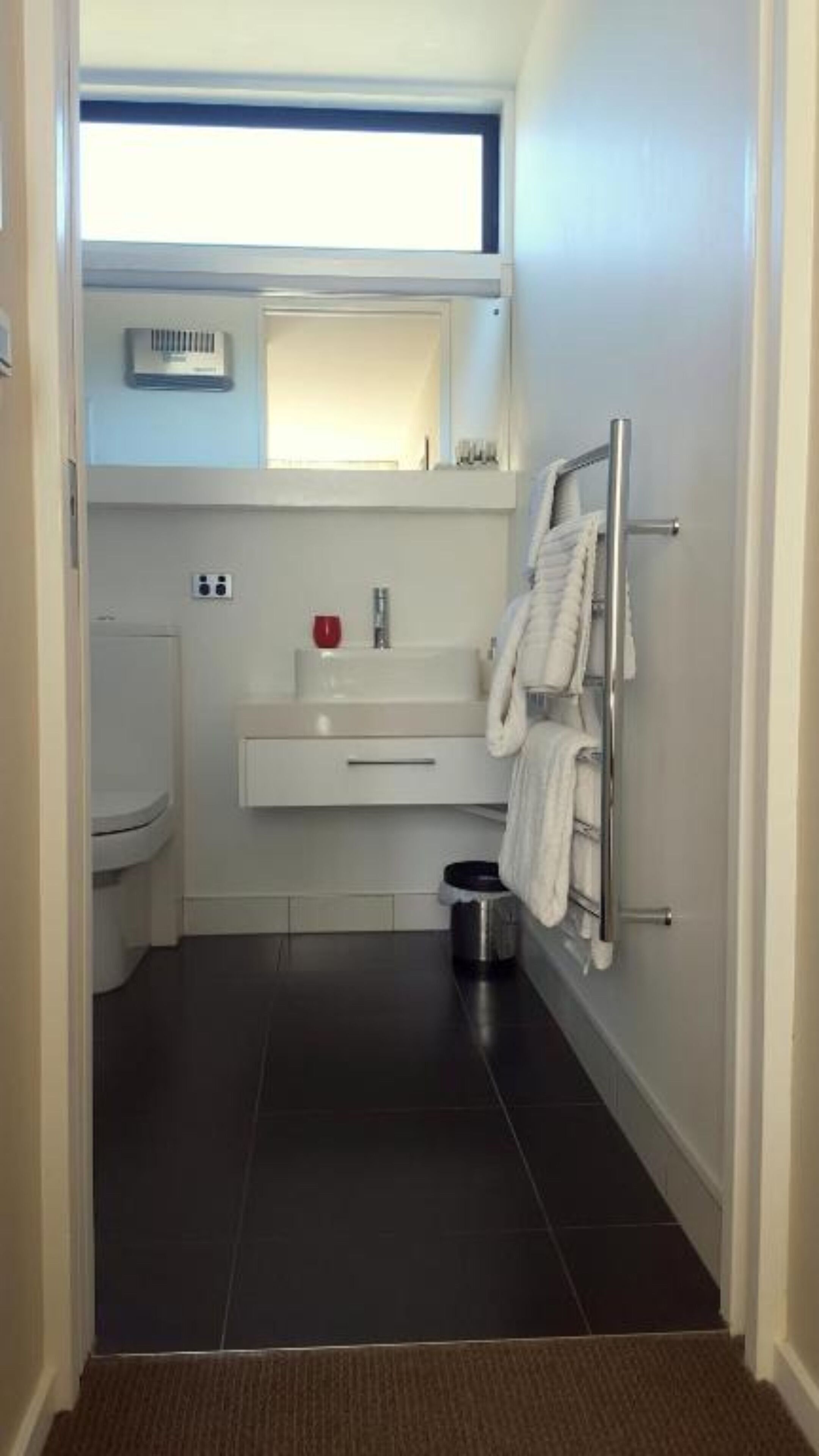 A modern bathroom with a white sink, mirror, and towel rack.