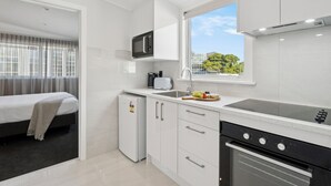 A compact kitchen with a microwave, toaster, sink, and oven. A bed is visible in the adjacent room. - Sai Motels - Greenlane Auckland (Auckland)