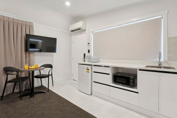 A modern kitchen with a flat-screen TV, a refrigerator, a microwave, and a dining area with two chairs and a table. - Sai Motels - Greenlane Auckland (Auckland)