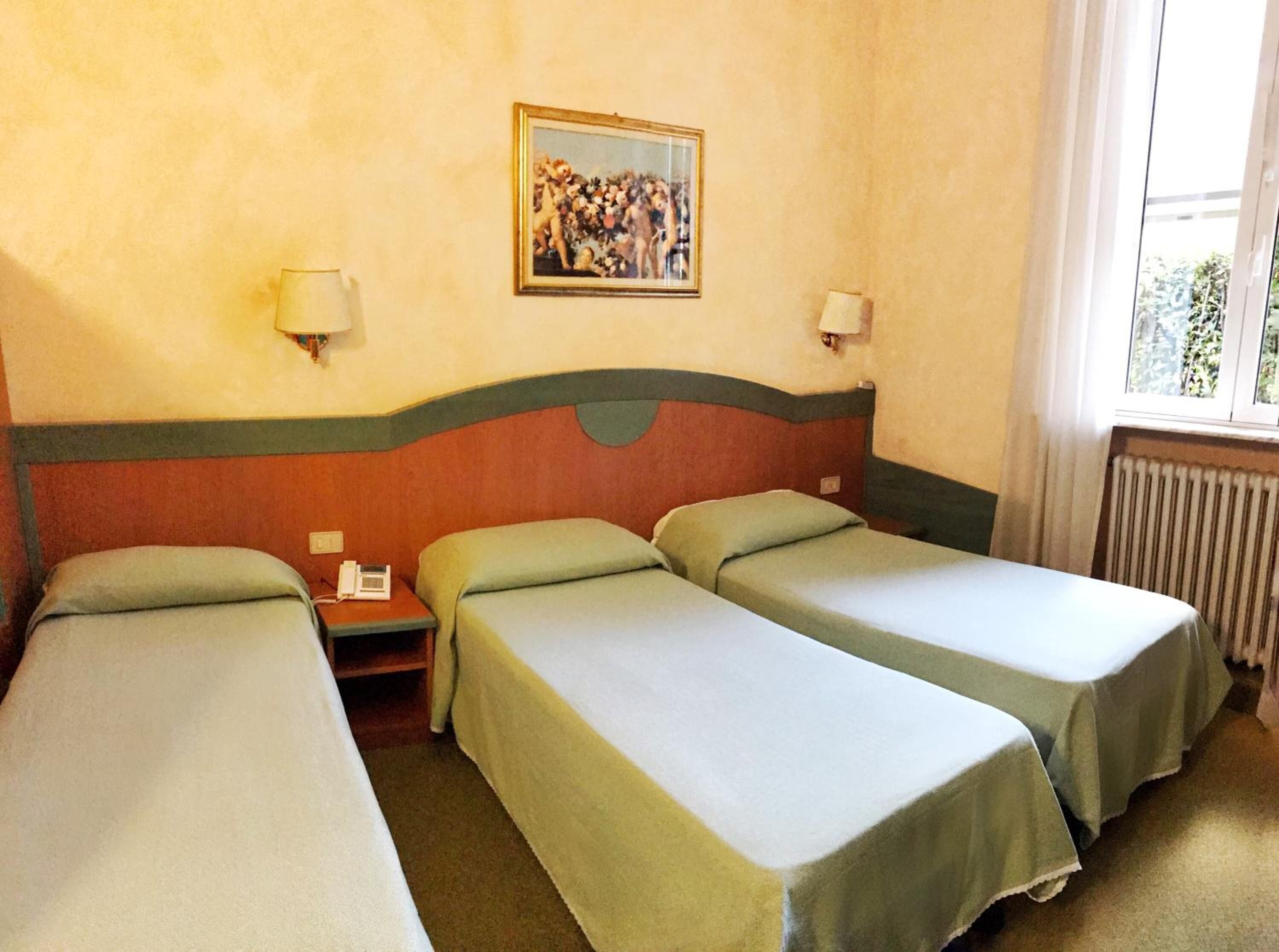 A hotel room with two single beds, a nightstand, a lamp, a painting on the wall, and a window with a view.