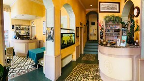 Vestíbulo de hotel con zona de bar, mostrador de recepción y escalera que sube a otro piso.