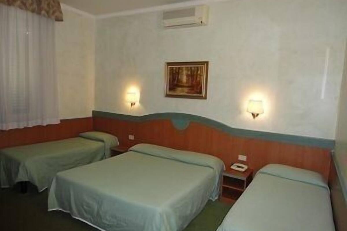 A hotel room with two single beds, a small table, and two wall-mounted lamps.