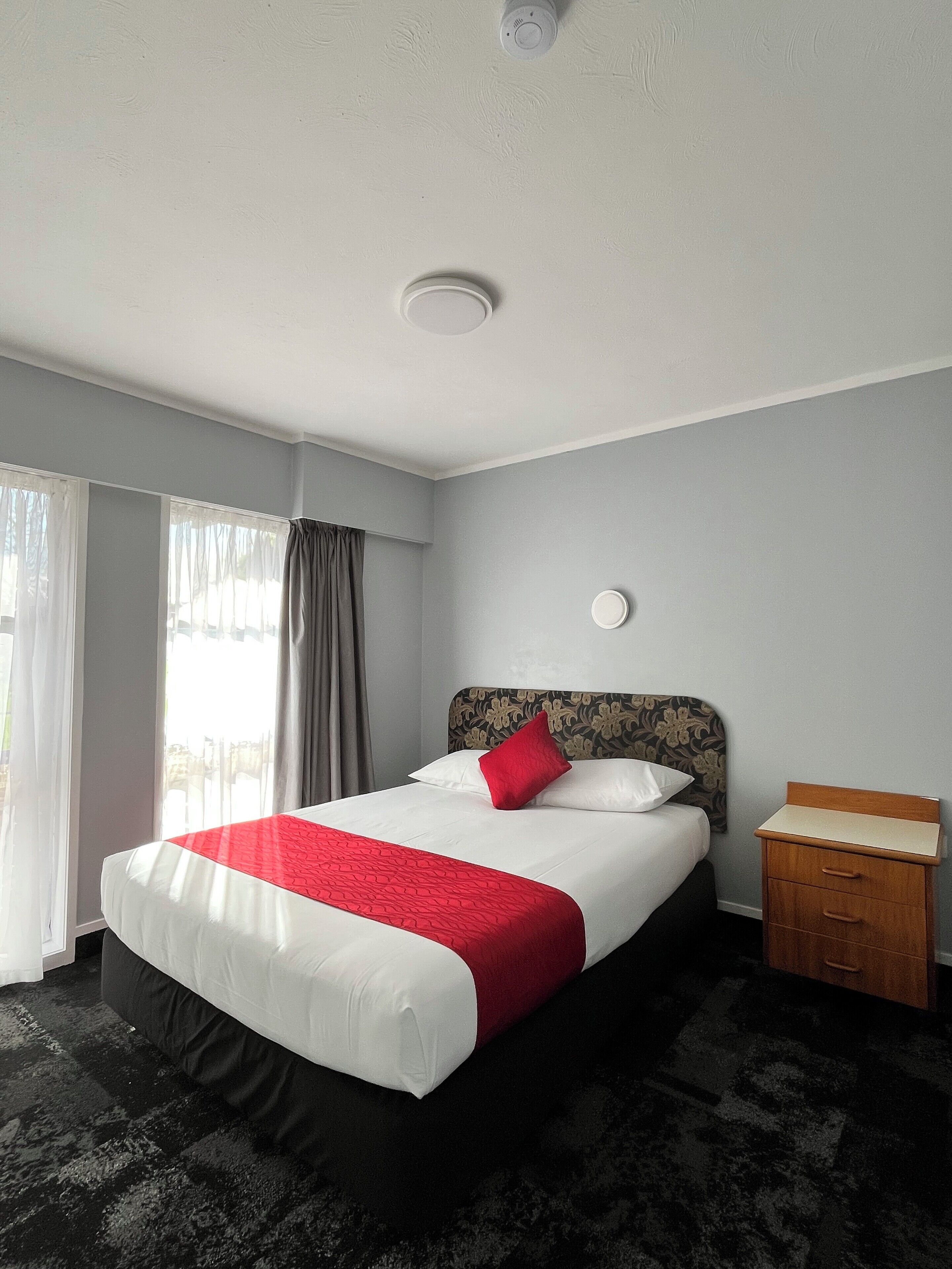 Een hotelkamer met een groot bed, een nachtkastje, een raam met gordijnen en een plafondlamp.