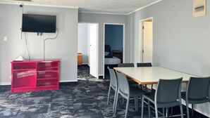 A room with a flat-screen TV mounted on the wall, a red storage unit, a dining table with four chairs, and a patterned carpet. - Beetham Park Motel (Hamilton)
