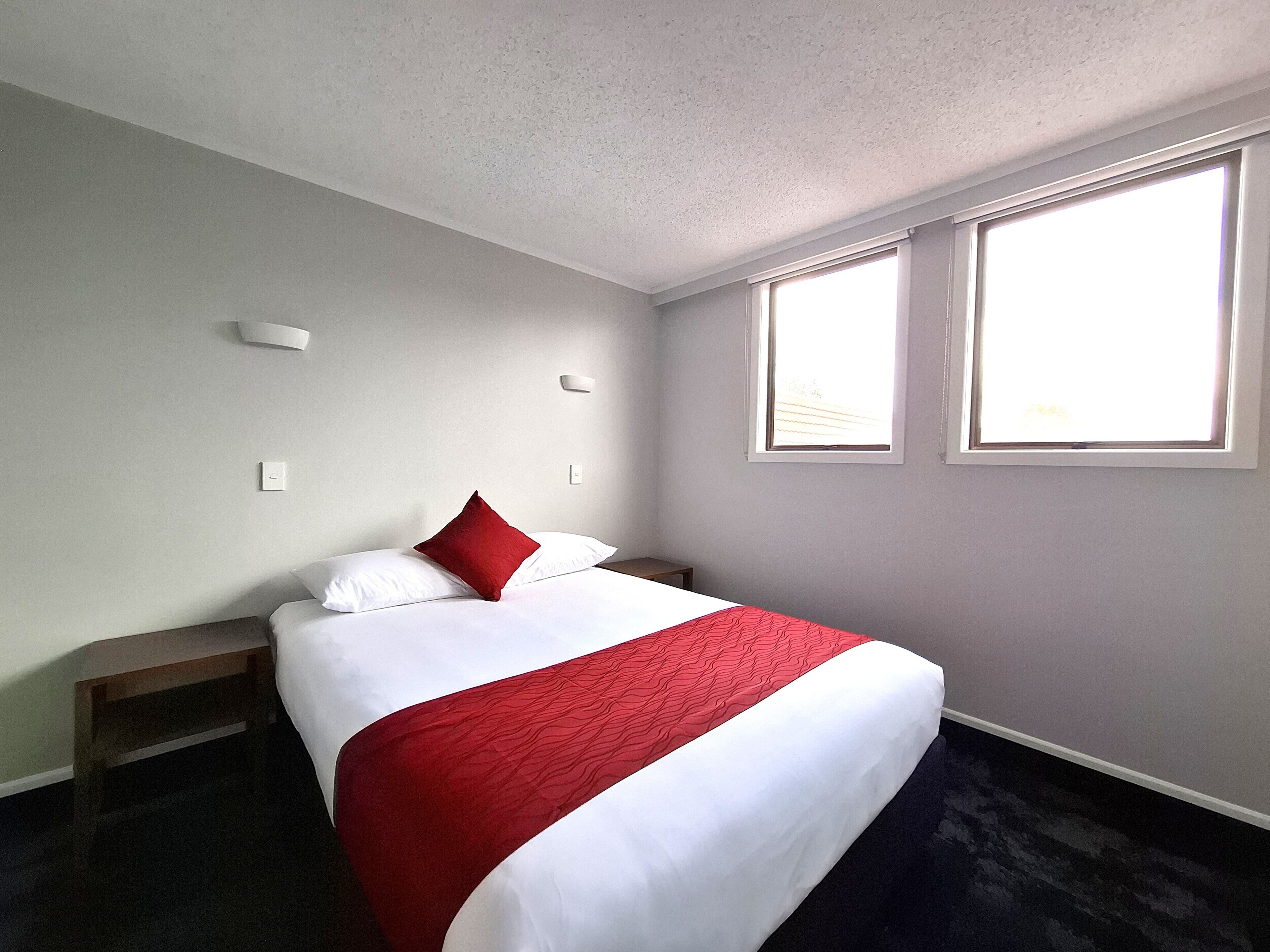 Une chambre d’hôtel avec un lit, une table de chevet, une fenêtre et une lampe fixée au mur.