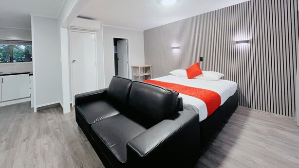 A modern hotel room with a bed, a black leather sofa, a small table, and a view of the outside. - Beetham Park Motel (Hamilton)