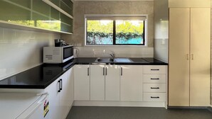 A modern kitchen with white cabinets, a black countertop, a microwave, a sink, and a window with a view of greenery. - Beetham Park Motel (Hamilton)