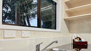 A modern kitchen with a stainless steel sink, a window with a view of trees, and a marble backsplash. - Beetham Park Motel (Hamilton)