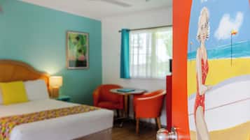 Habitación de hotel con cama, escritorio, silla y un cuadro de una playa.