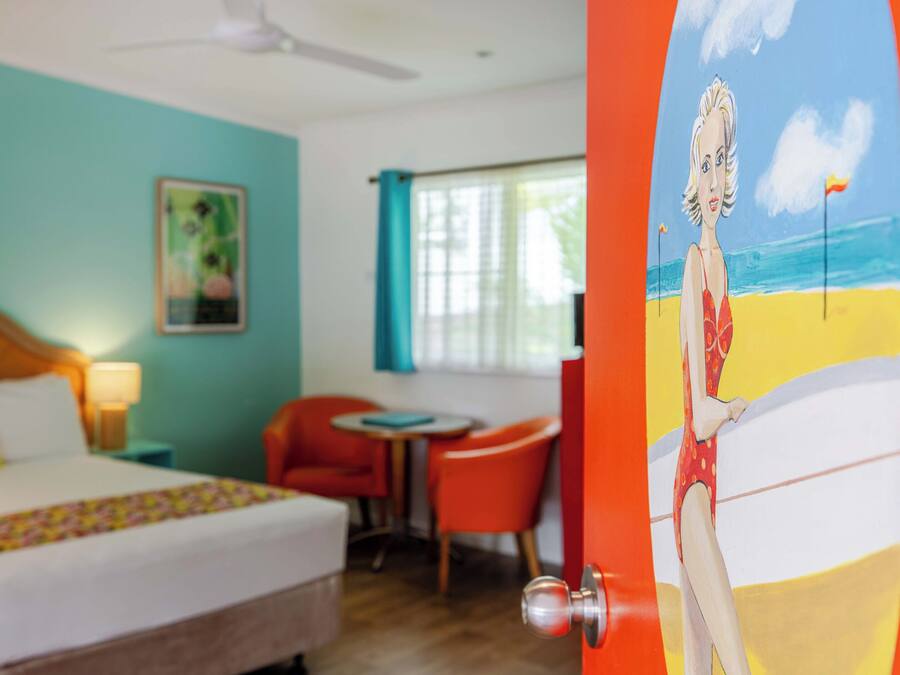 Een hotelkamer met een bed, een bureau, een stoel en een schilderij van een strand.