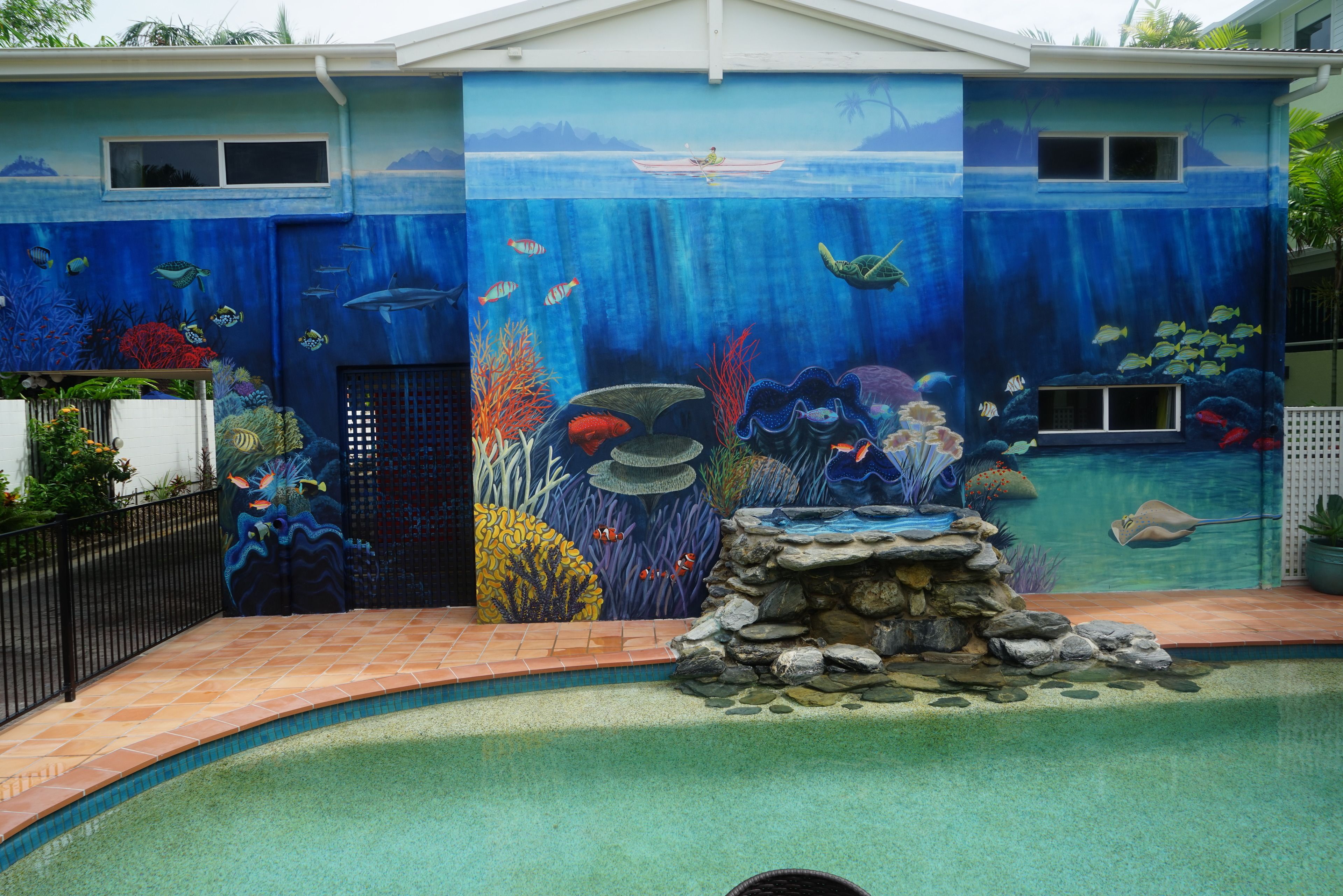 A house with a mural of an underwater scene on the exterior wall, a swimming pool, and a small waterfall feature.
