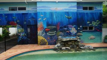 Une maison dont la façade extérieure est ornée d’une fresque représentant un paysage sous-marin, avec une piscine et une petite cascade.