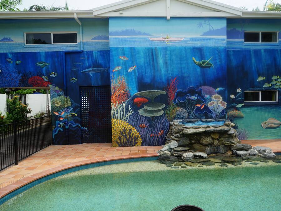 Une maison dont la façade extérieure est ornée d’une fresque représentant un paysage sous-marin, avec une piscine et une petite cascade.