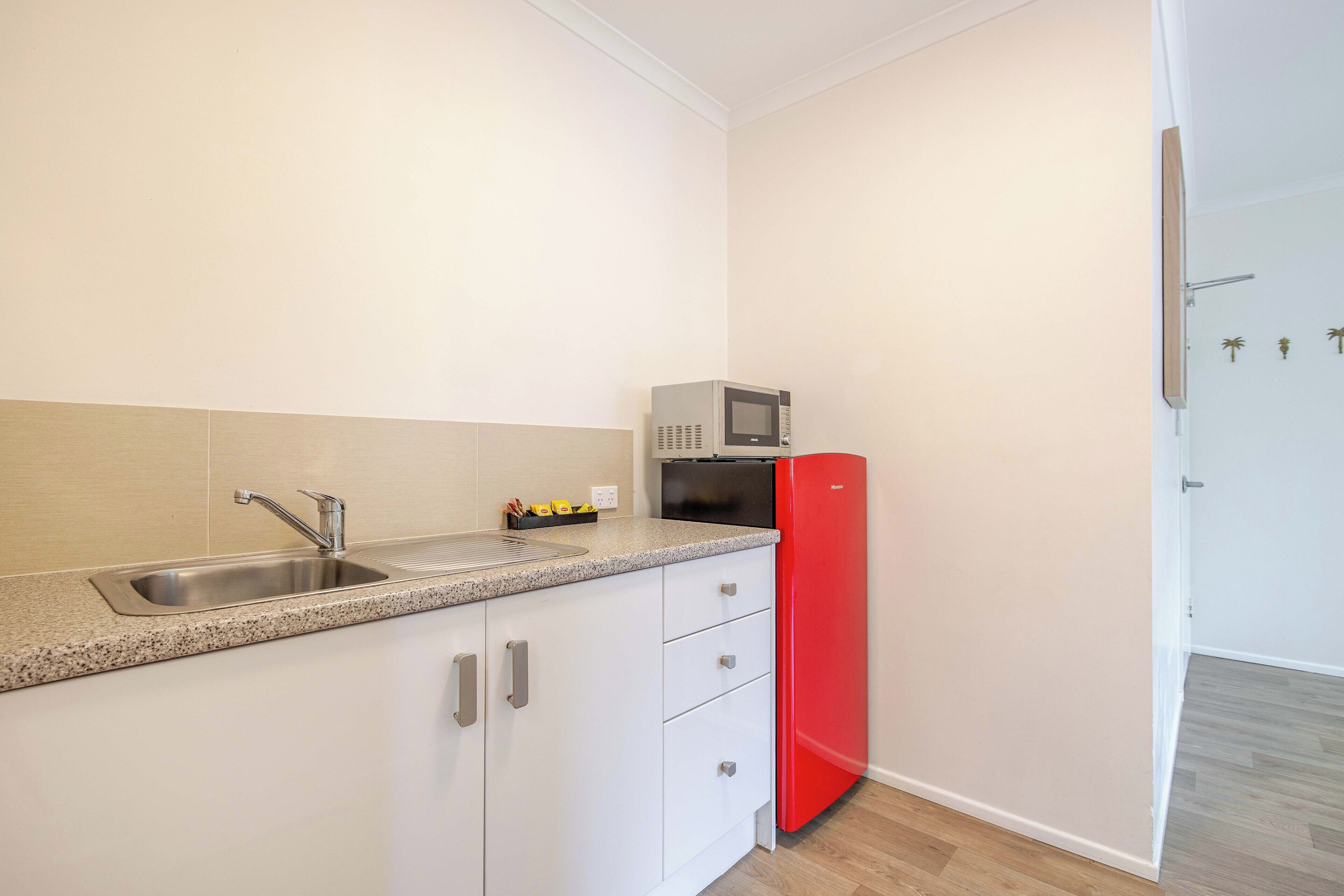 A kitchen with a stainless steel sink, a microwave, and a red refrigerator.
