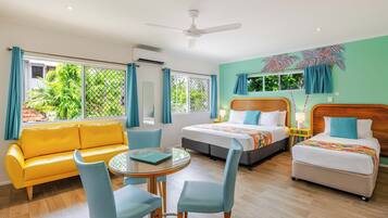 A hotel room with a yellow sofa, two beds, a dining table with chairs, and large windows with curtains.