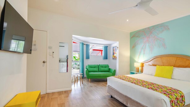 A hotel room with a bed, a green sofa, a yellow table, and a ceiling fan. - Port Douglas Motel (Port Douglas)