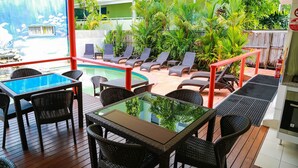 A poolside area with lounge chairs, a glass table, and a view of a pool and greenery. - Port Douglas Motel (Port Douglas)