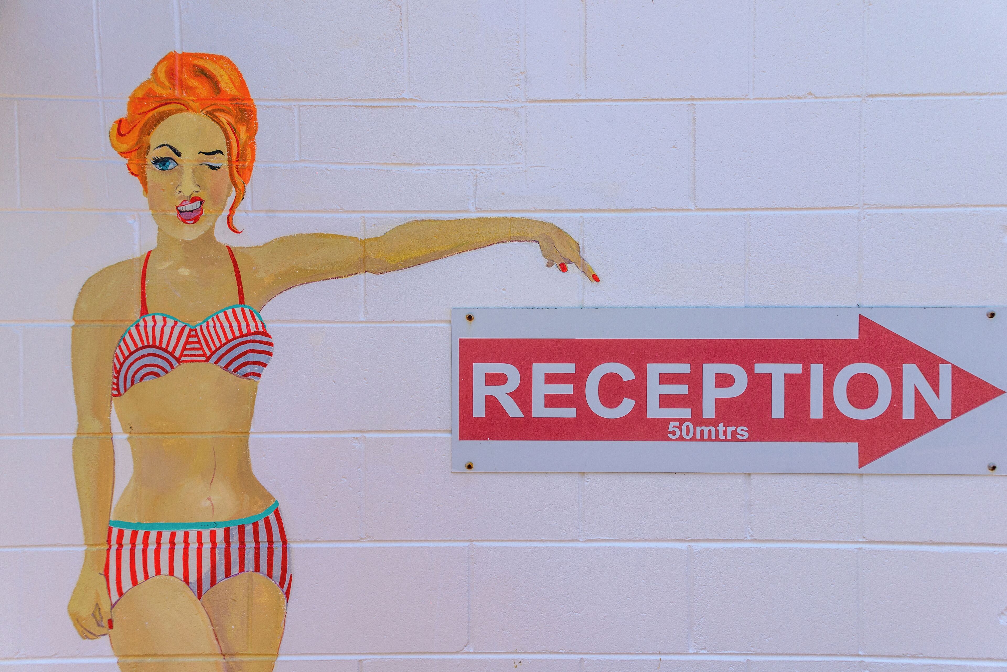 A wall with a reception sign and a mural of a woman in a bikini pointing towards the sign.
