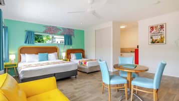 A hotel room with two beds, a dining table with chairs, a ceiling fan, and a kitchen area.