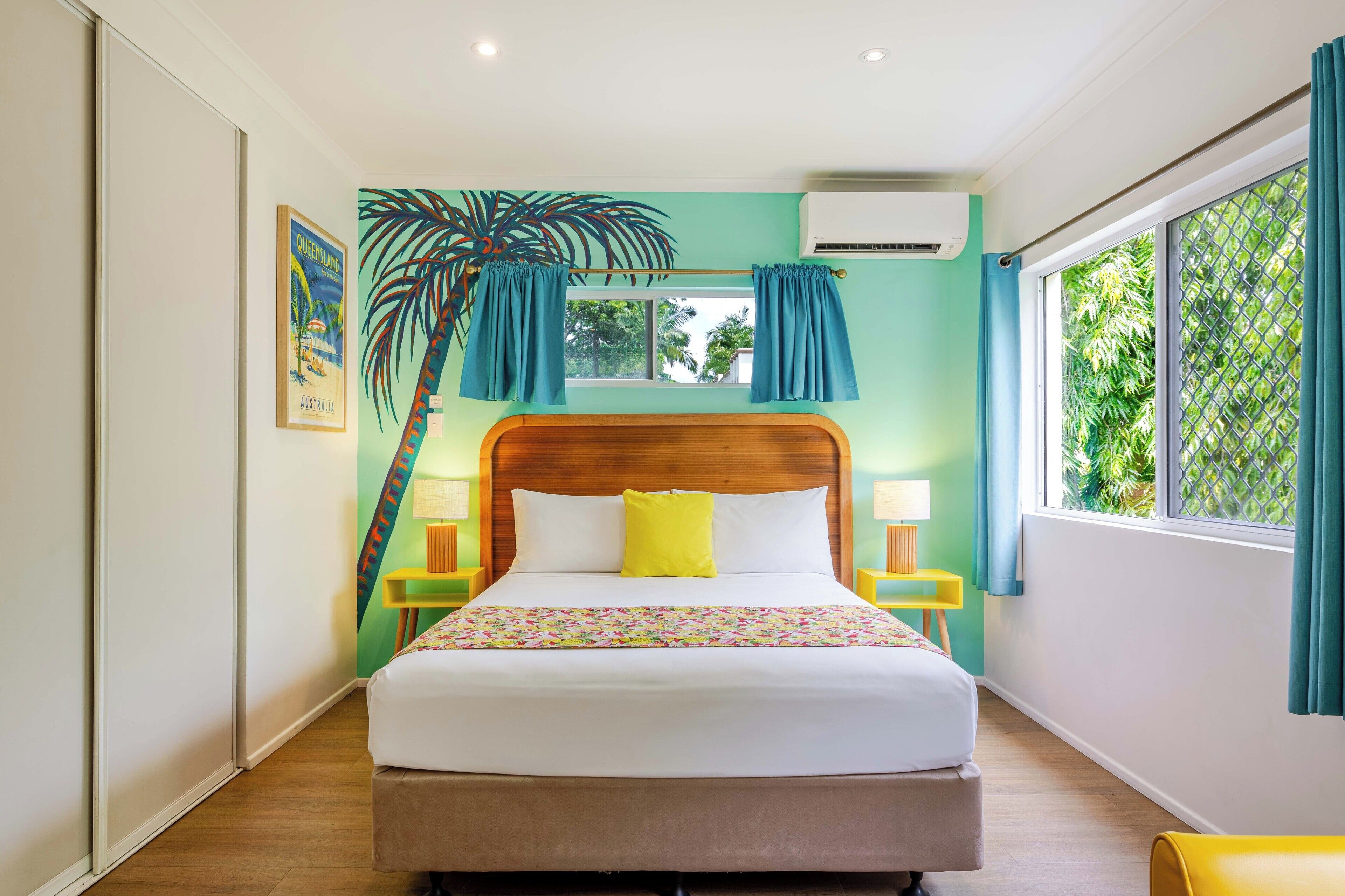 A bedroom with a bed, a window with curtains, a wall-mounted air conditioner, and a framed picture on the wall.