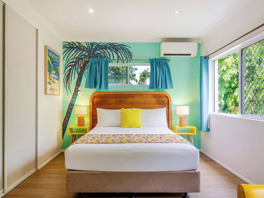 Une chambre à coucher avec un lit, une fenêtre avec des rideaux, un climatiseur fixé au mur et un tableau encadré accroché au mur.