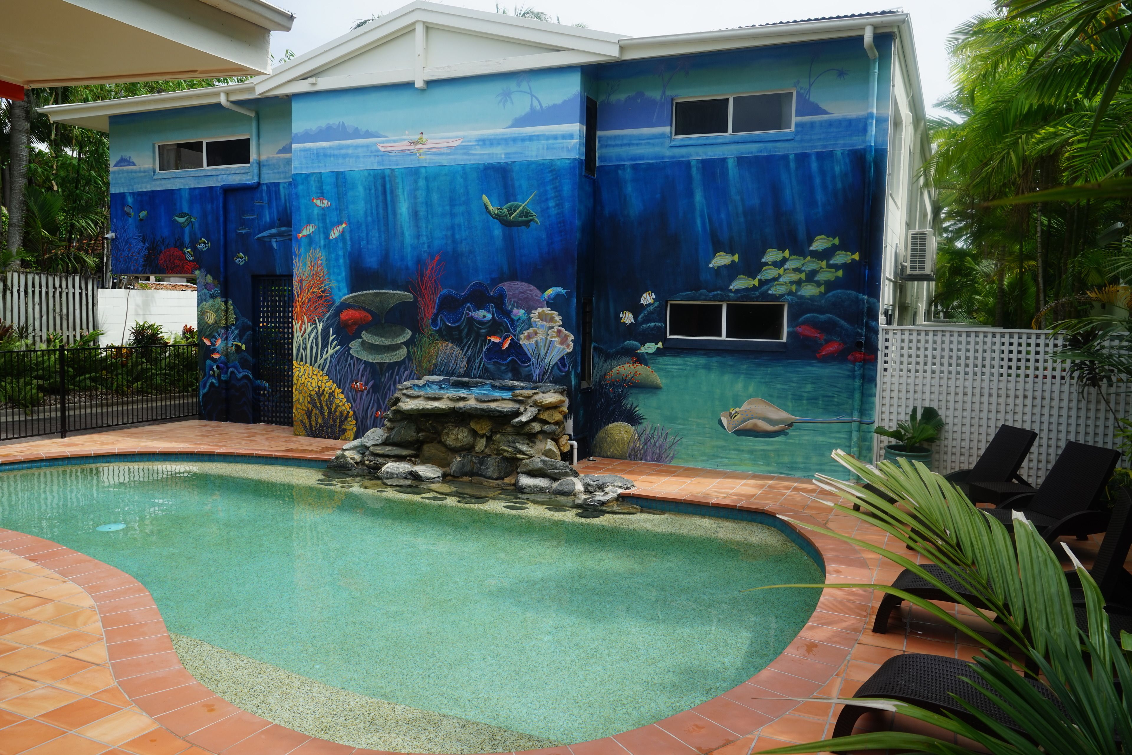 A swimming pool with a mural of an underwater scene, surrounded by a patio area with lounge chairs.