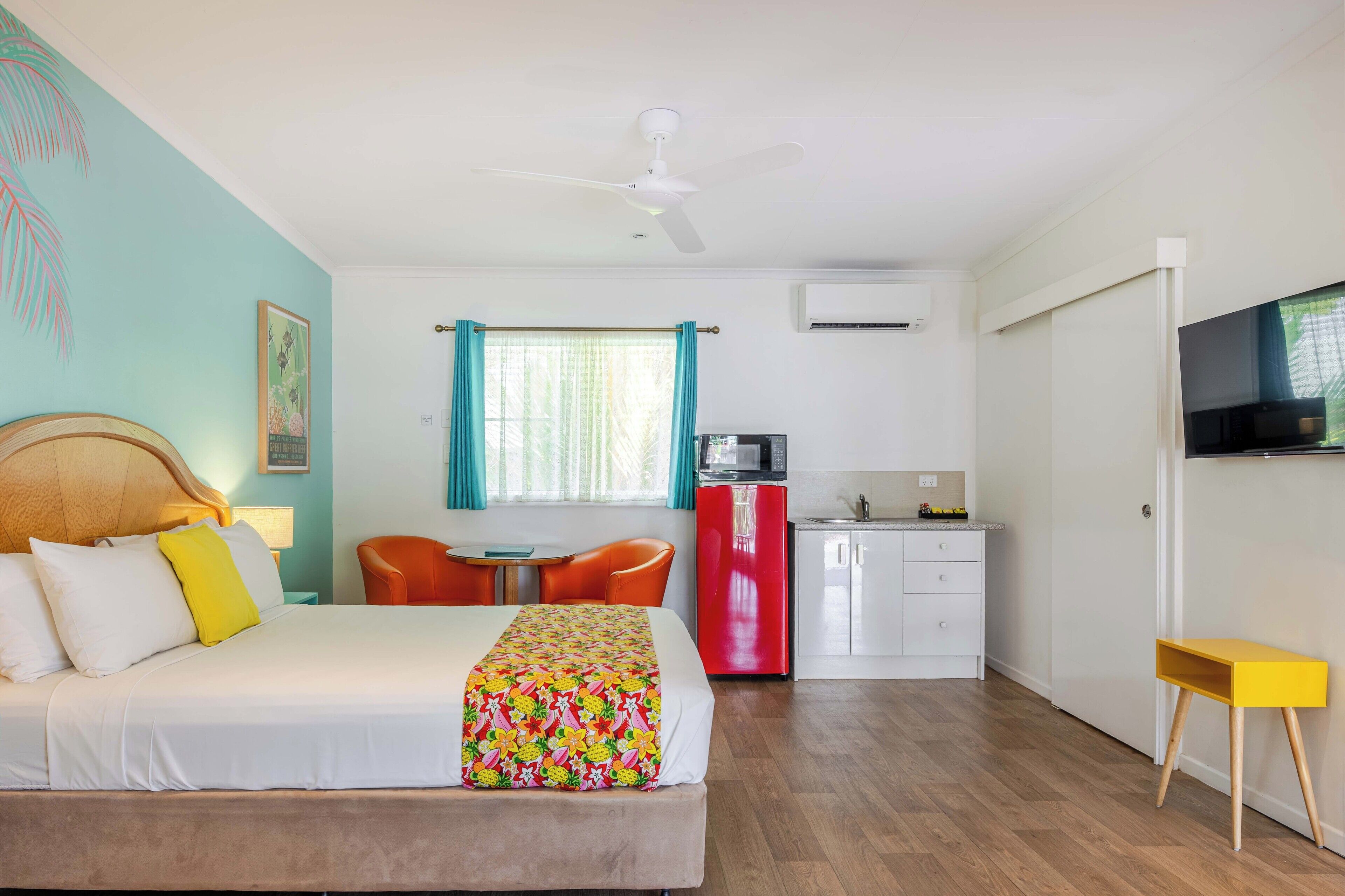 A hotel room with a bed, a desk, a chair, a microwave, a refrigerator, and a television.