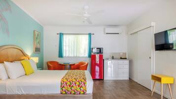 A hotel room with a bed, a desk, a chair, a microwave, a refrigerator, and a television.