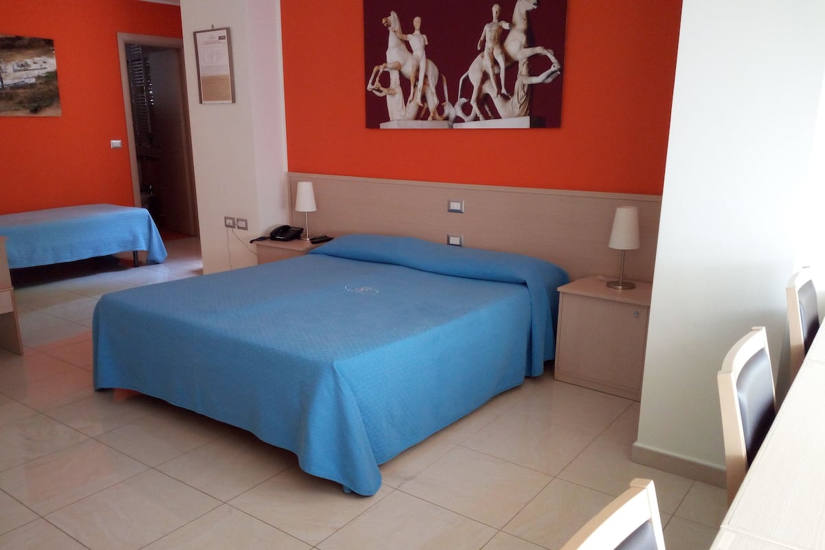 A hotel room with two beds, a desk, a chair, a telephone, and a painting on the wall.