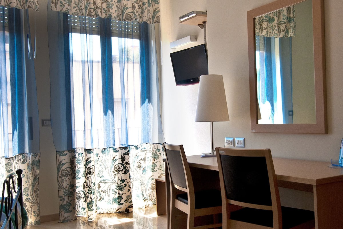 A hotel room with a desk, chairs, a television, a lamp, and a large mirror.