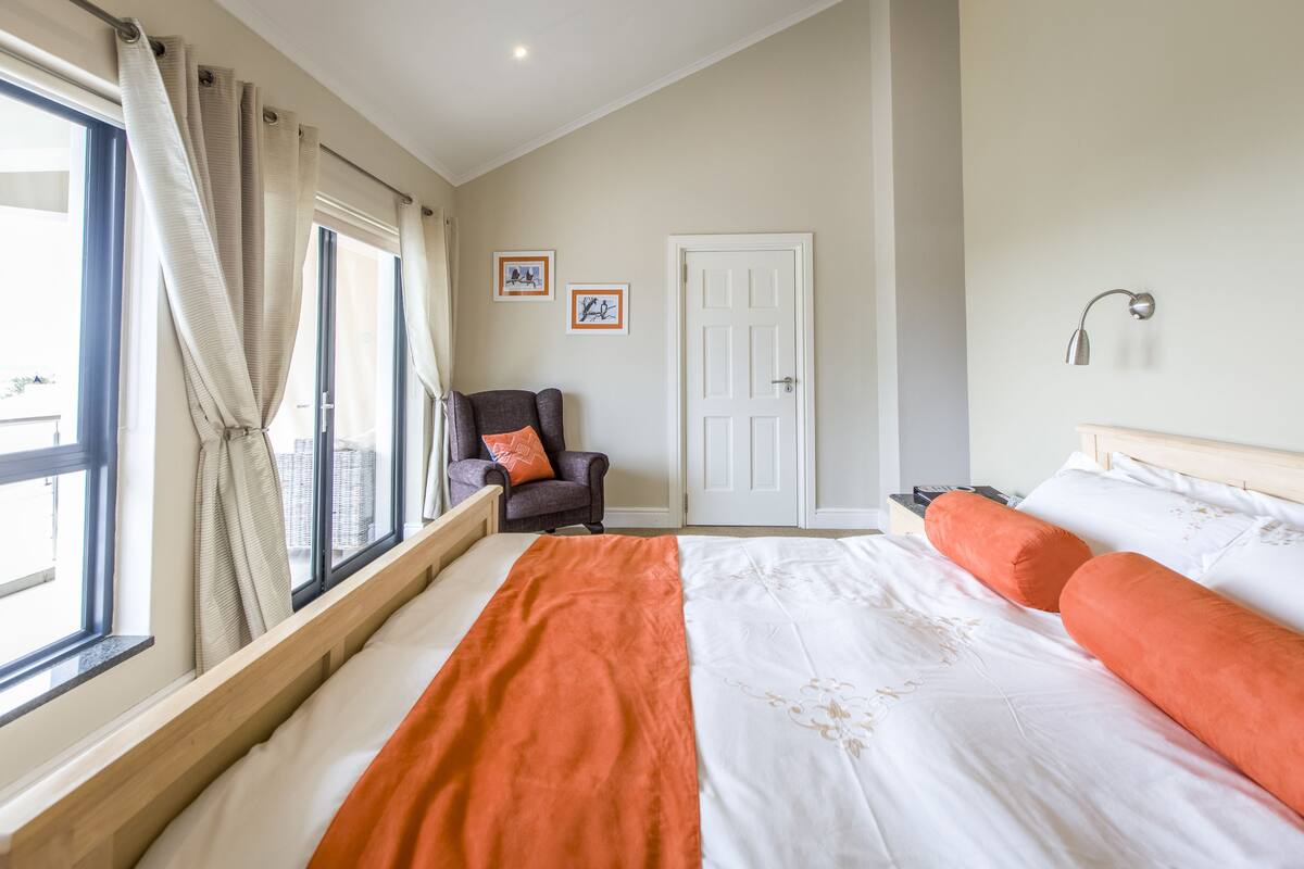 A hotel room with a large bed, a chair, a door, and a window with curtains.