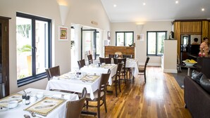 A spacious dining area with multiple tables set for service, a kitchen area visible in the background, and large windows providing natural light. - Orange Inn Knysna (Knysna)