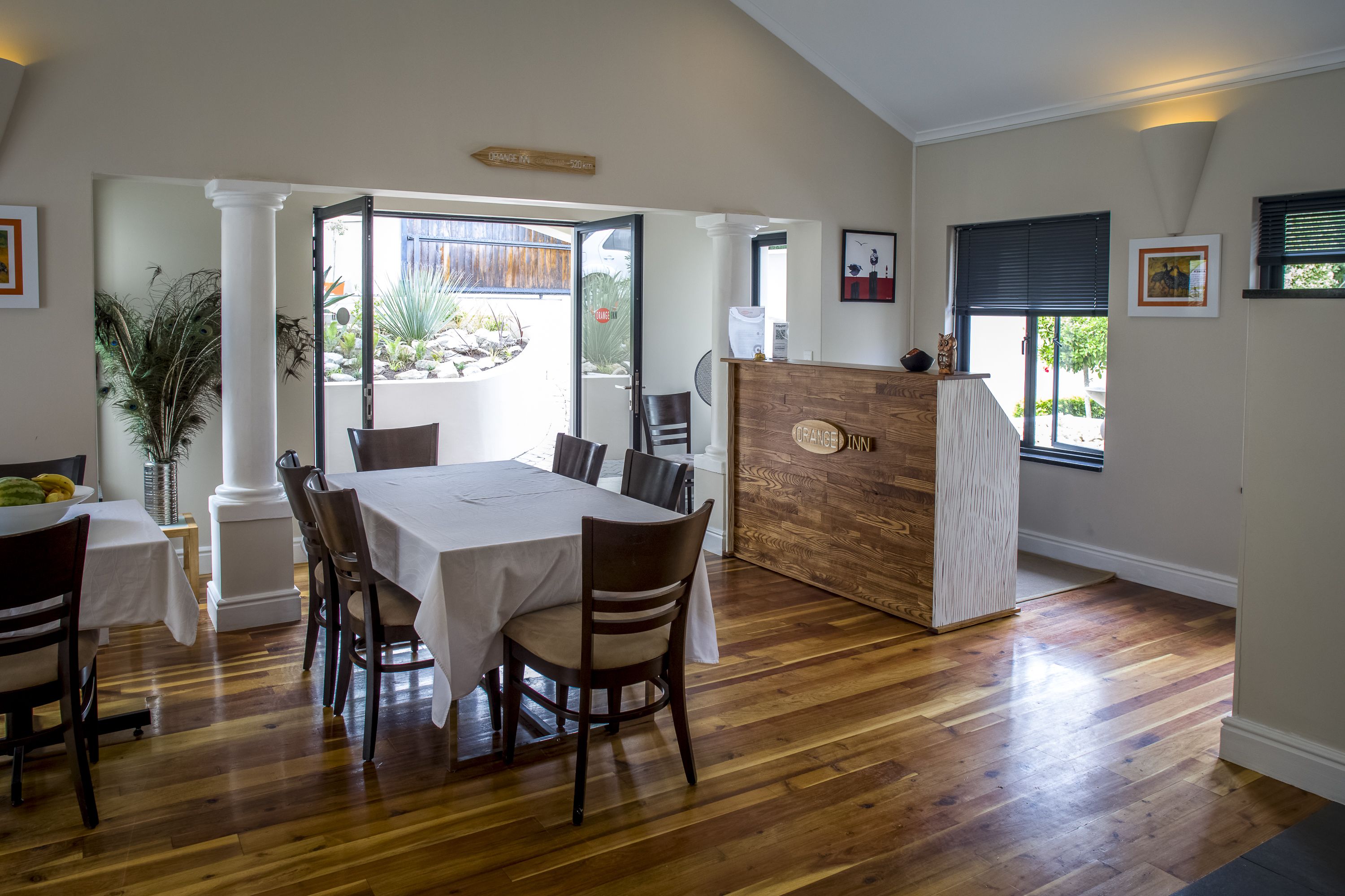 A dining area with a wooden table and chairs, a reception desk, and a view of the outdoors.