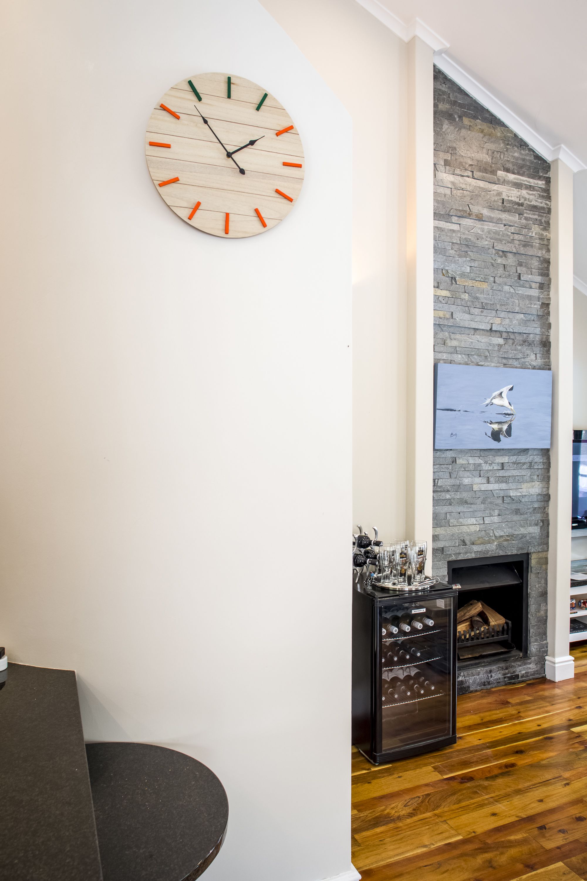 A living room with a wooden clock, a stone fireplace, and a wine cooler.
