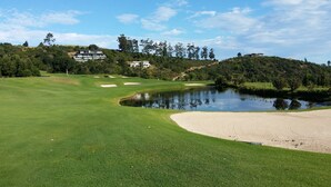 A golf course with a pond, sand bunkers, and a clubhouse in the background. - Orange Inn Knysna (Knysna)