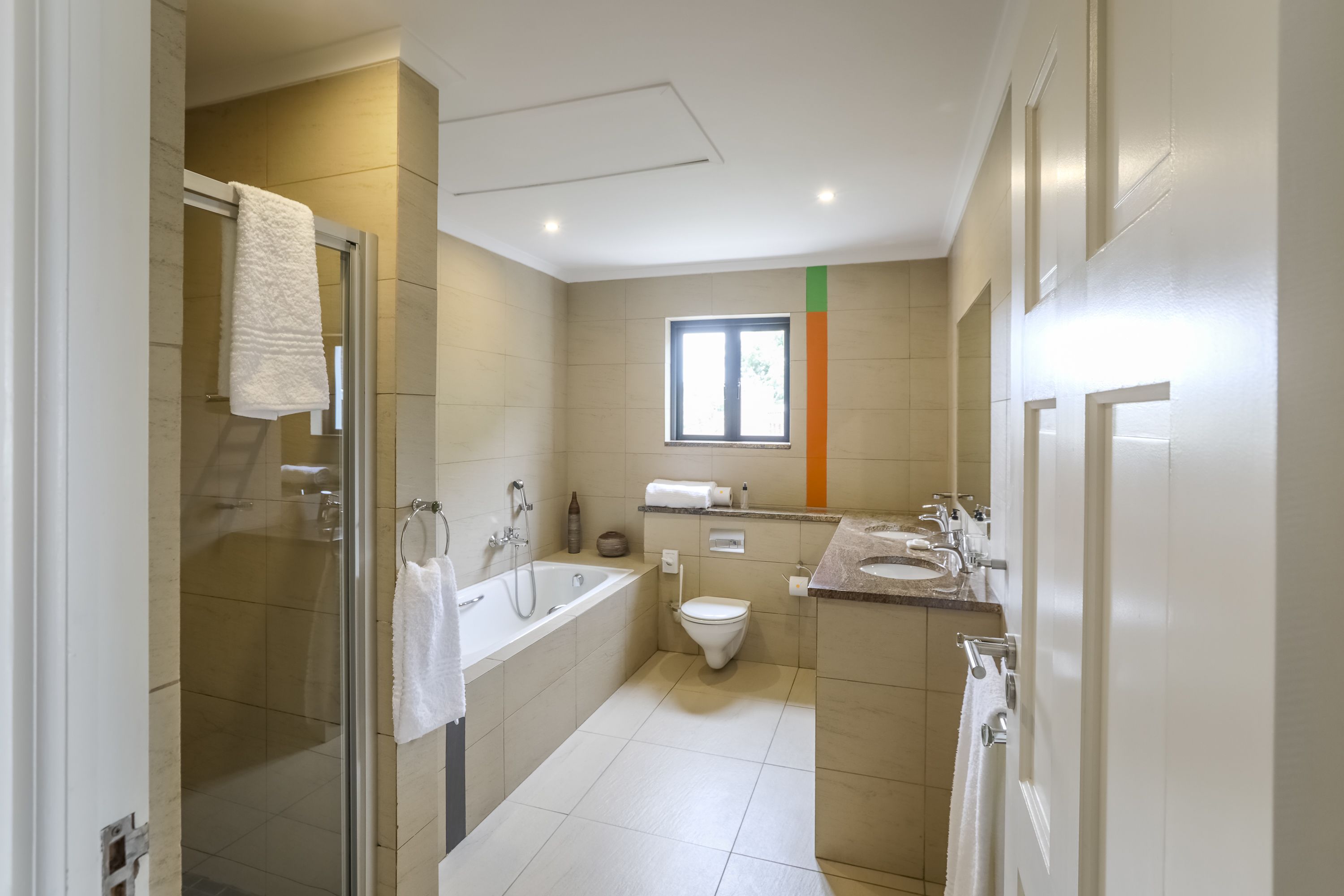 Et moderne badeværelse med brusekabine i glas, badekar, toilet og håndvask.
