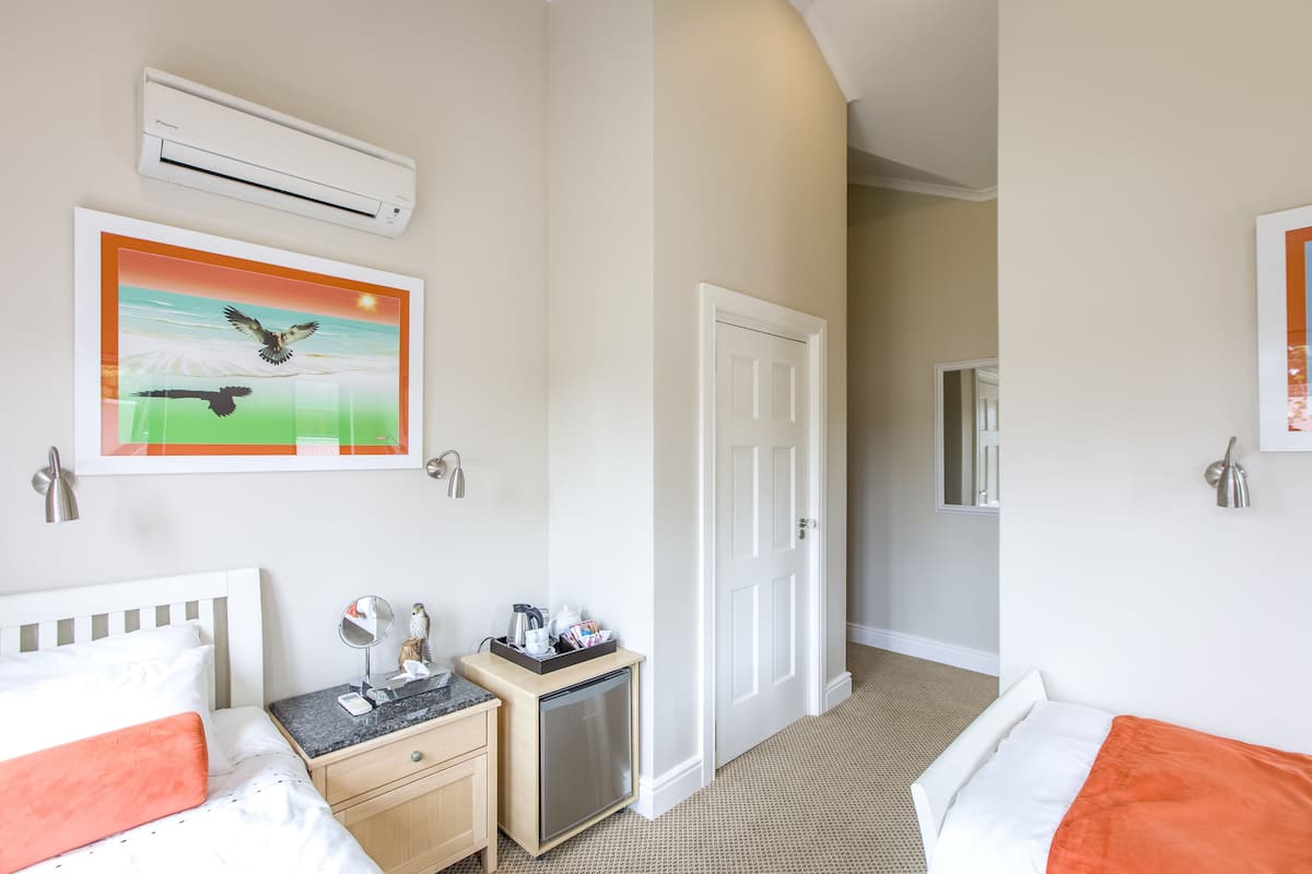 A hotel room with two beds, a small kitchenette, a door leading to another room, and a framed picture on the wall.