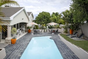 Una piscina con sillones de descanso y sombrillas, rodeada de vegetación y un edificio moderno.