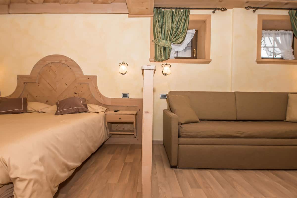 Un dormitorio con una cama, un sofá, dos mesitas de noche y dos lámparas de pared.