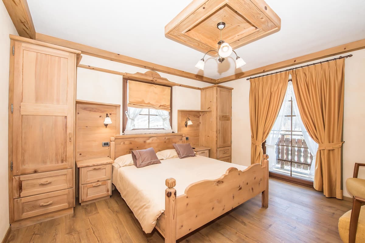 Un dormitorio de madera con cama, mesitas de noche, un armario y una ventana con cortinas.