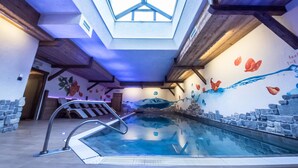 An indoor swimming pool with a skylight, stone walls, and a mural with aquatic themes. - Hotel Capriolo (Livigno)