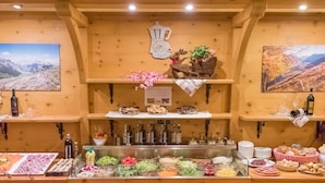 A buffet setup with various food items, including meats, cheeses, and salads, in a wooden interior with mountain views. - Hotel Capriolo (Livigno)