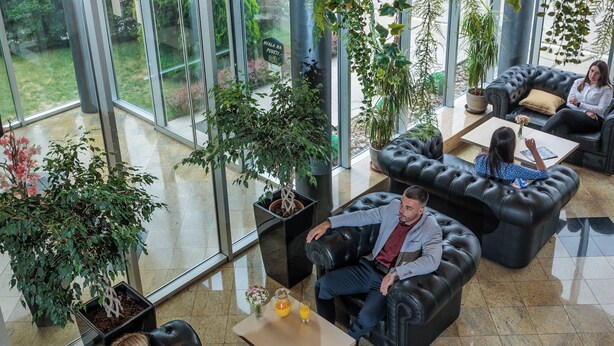 A modern lounge area with leather sofas, potted plants, and large windows offering a view of the outdoors. - Euro Garni Hotel (Belgrade)