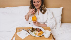 A person sitting on a bed with a tray containing breakfast items and a drink. - Euro Garni Hotel (Belgrade)