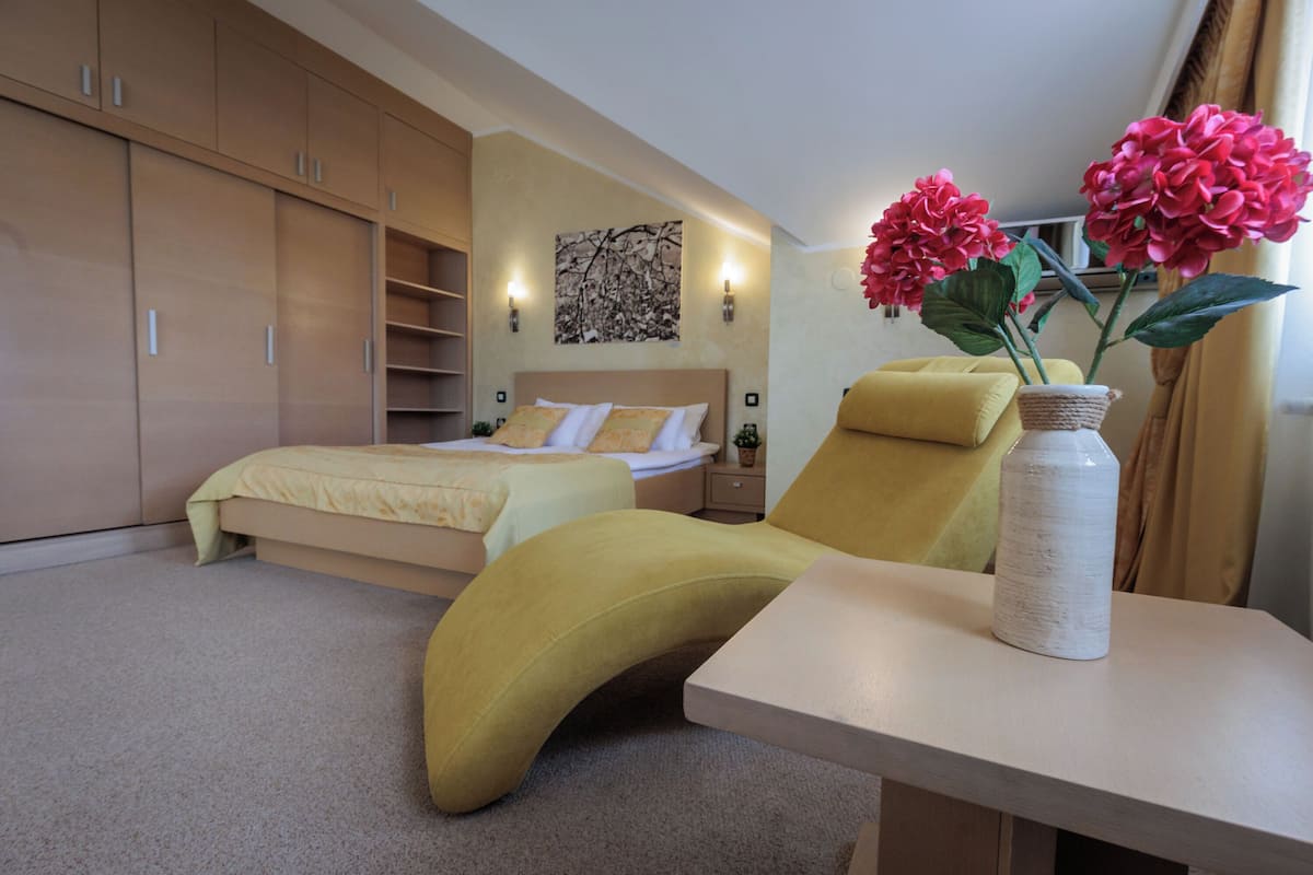 A modern bedroom with a bed, a yellow armchair, a bedside table with a vase of flowers, and a large wardrobe.