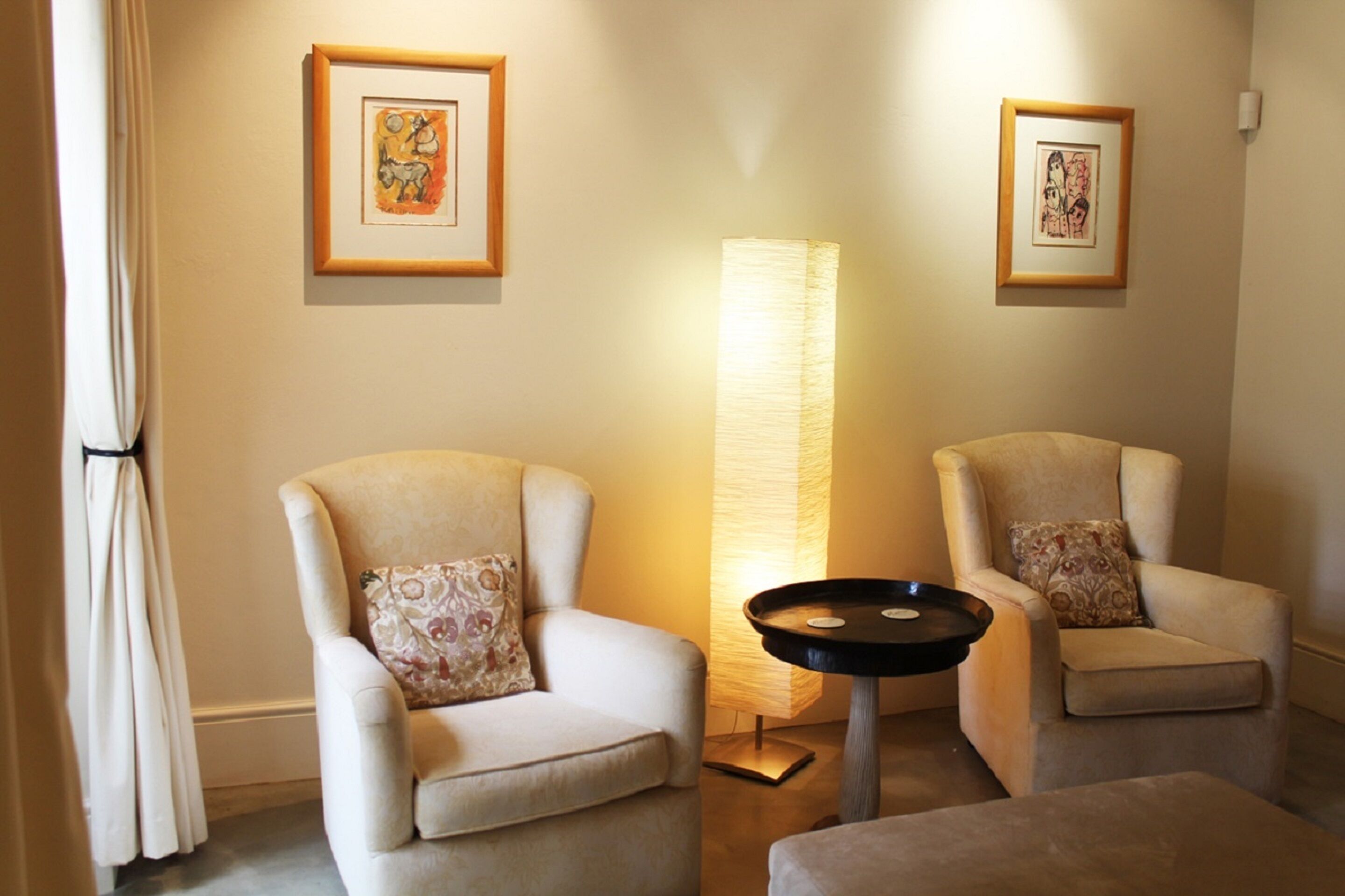 A room with two armchairs, a floor lamp, and framed artwork on the walls.