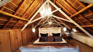 Une chambre à coucher avec un plafond en bois en forme de voûte, un lit recouvert de nombreux coussins et un lustre.
