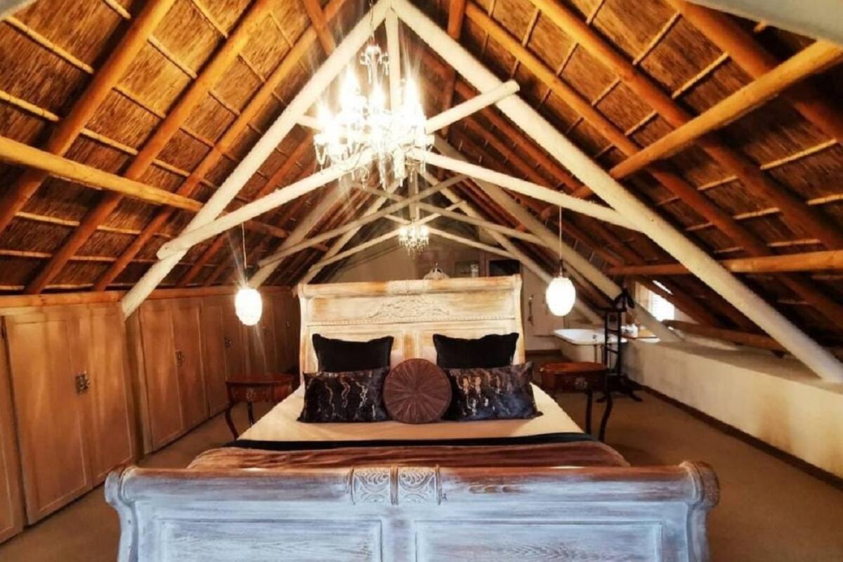 Une chambre à coucher avec un plafond en bois en forme de voûte, un lit recouvert de nombreux coussins et un lustre.